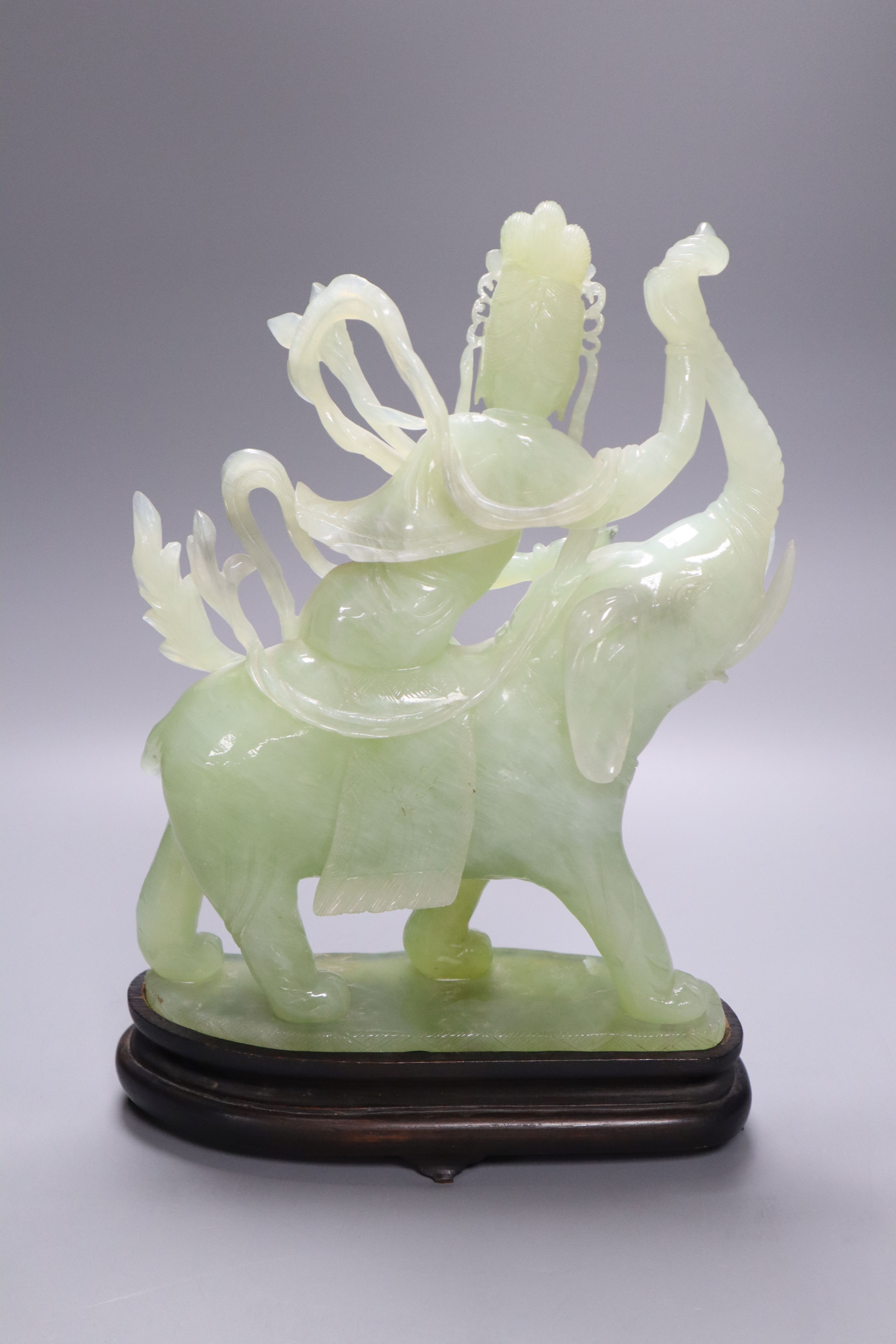 A Chinese bowenite jade group of Guanyin riding on elephant, 27cm high, wood stand